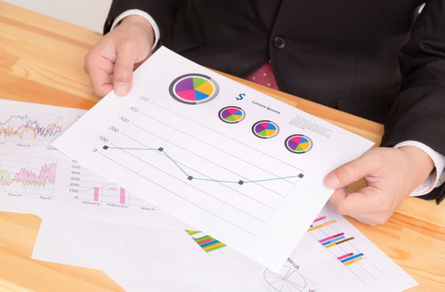 グラフ資料を両手で持って見せるスーツの男性