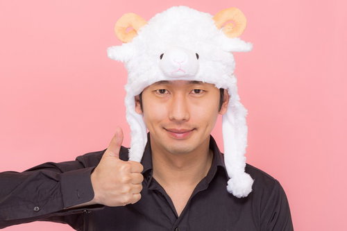 ピンク背景で羊の帽子を被り親指を立てる黒シャツの男性