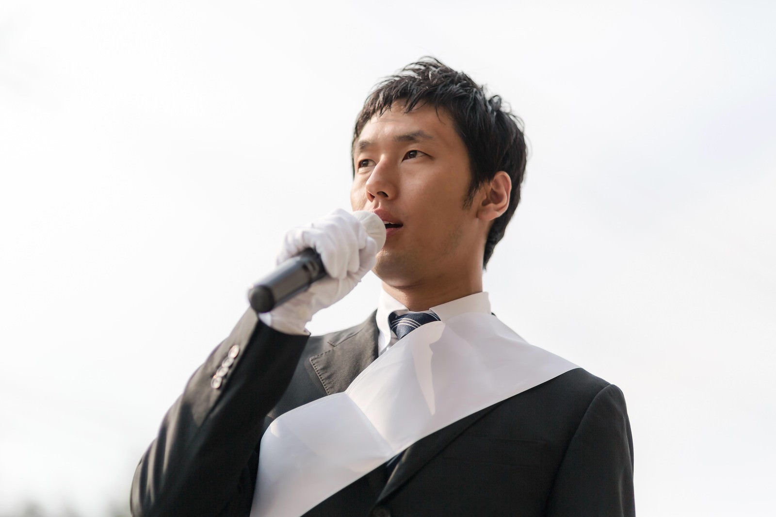 街宣車の上からマイクで演説する立候補者［モデル：大川竜弥］
