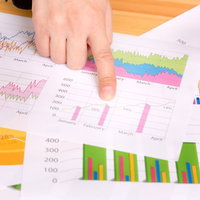 テーブルに広げたグラフ資料を指差す手の写真