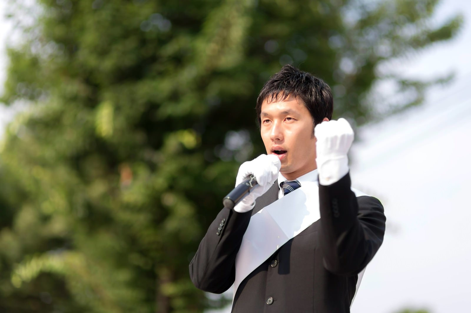 拳を上げてマイクで訴える白い手袋の立候補者［モデル：大川竜弥］