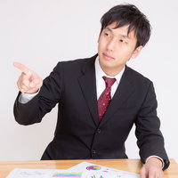 机に広げた資料を指差して問題を指摘する男性の写真