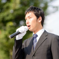 白い手袋でマイクを握り街頭演説する男性の写真