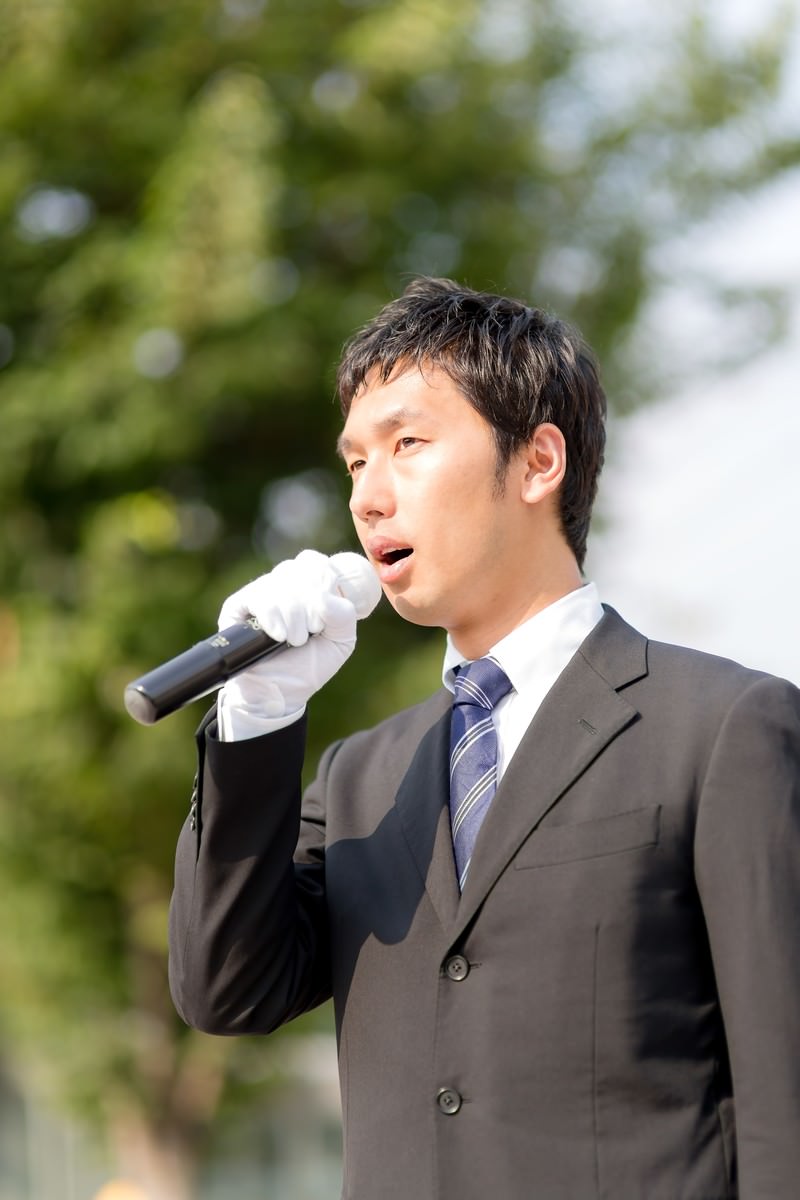 街頭演説でマイクを持って政策を主張する若い男性立候補者［モデル：大川竜弥］