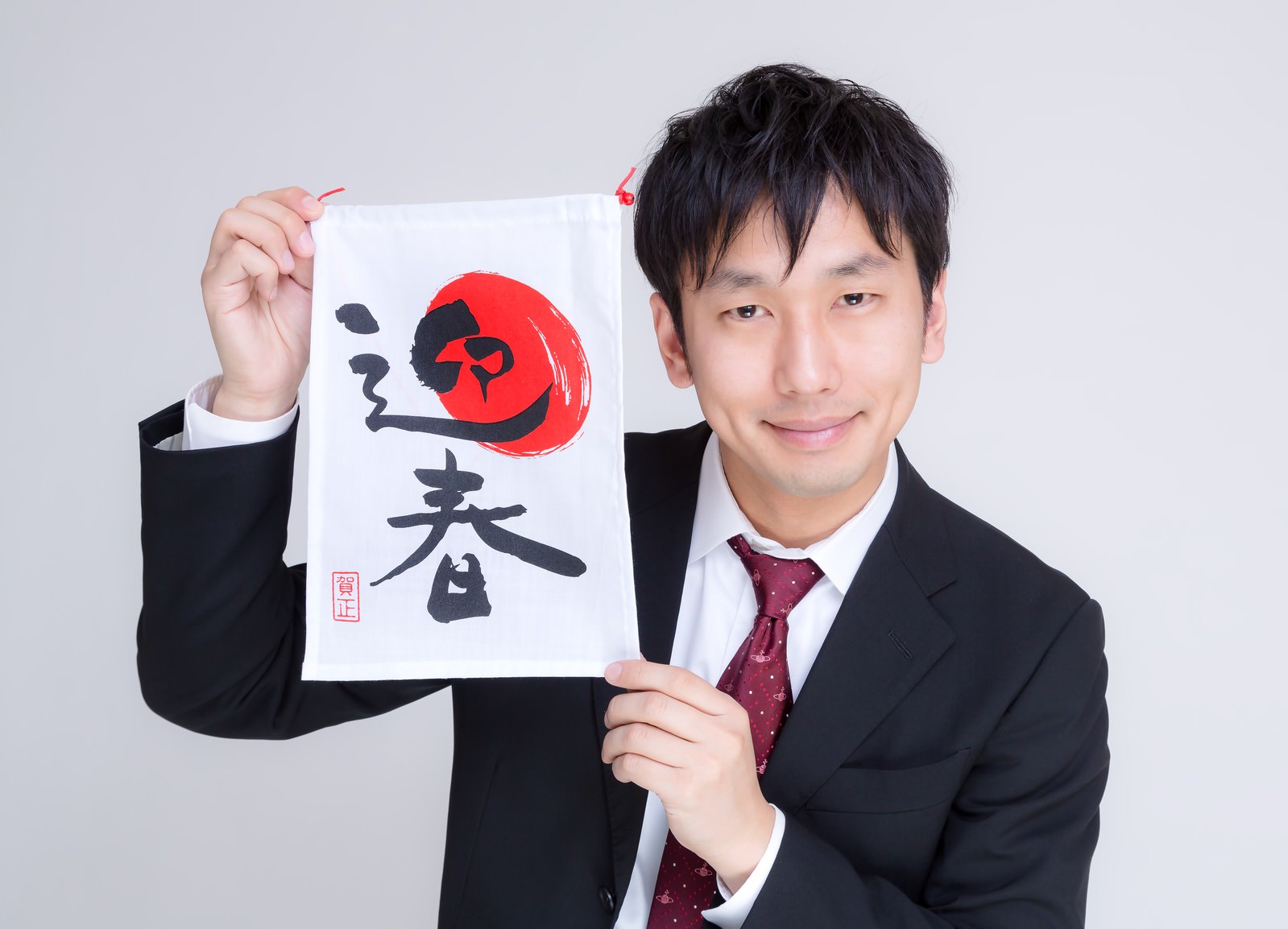 迎春の巾着を掲げるスーツの男性［モデル：大川竜弥］