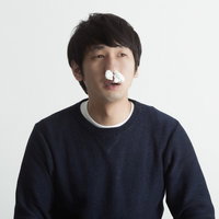 紺色のセーターで鼻に白いティッシュを詰めた黒髪の人物の写真