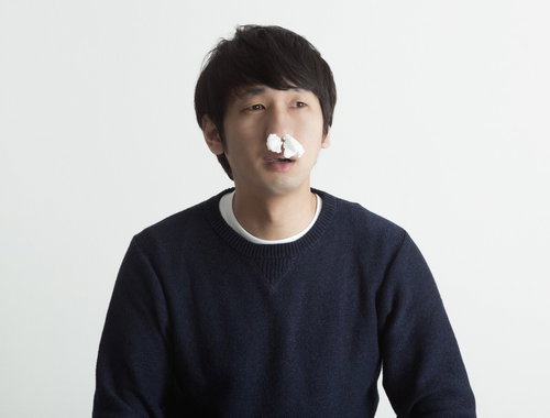 紺色のセーターで鼻に白いティッシュを詰めた黒髪の人物