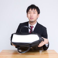 札束に見立てた白い箱がかばんに入ったと説明するビジネスマンの写真