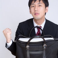 バッグを掲げてガッツポーズするスーツの男性の写真