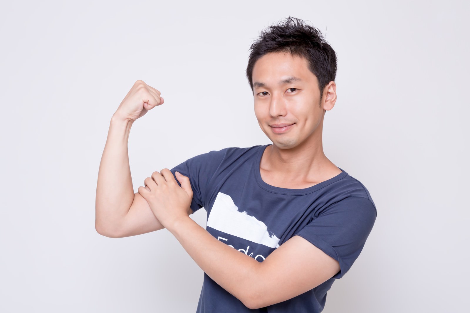 力こぶを見せながら笑顔でポーズをする紺色のTシャツを着た男性［モデル：大川竜弥］