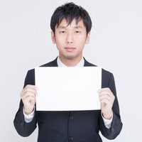 白い紙を胸の前に持つスーツの男性の写真