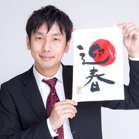 筆文字の「迎春」を掲げるスーツの男性の写真