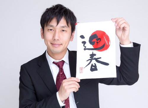 筆文字の「迎春」を掲げるスーツの男性