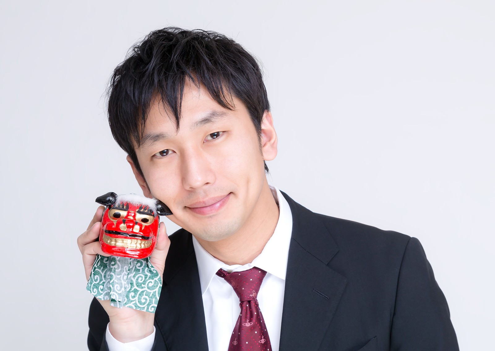 紺色のスーツを着た男性が赤い獅子舞の面を肩に持つ［モデル：大川竜弥］