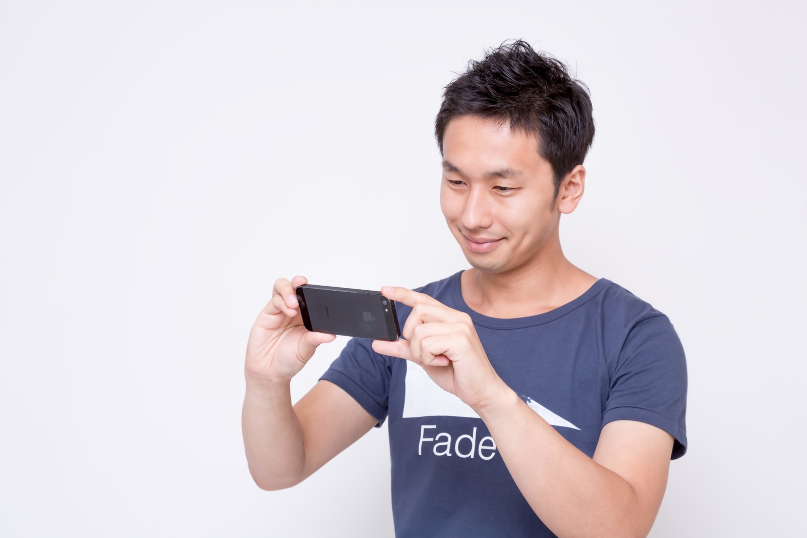 スマートフォンを横向きに持って撮影する紺色のTシャツを着た男性［モデル：大川竜弥］