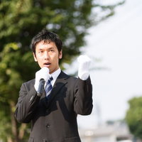屋外でマイクと紙を持って演説するスーツの男性の写真