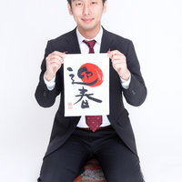 正座して「迎春」の書を掲げるスーツのビジネスマンの写真