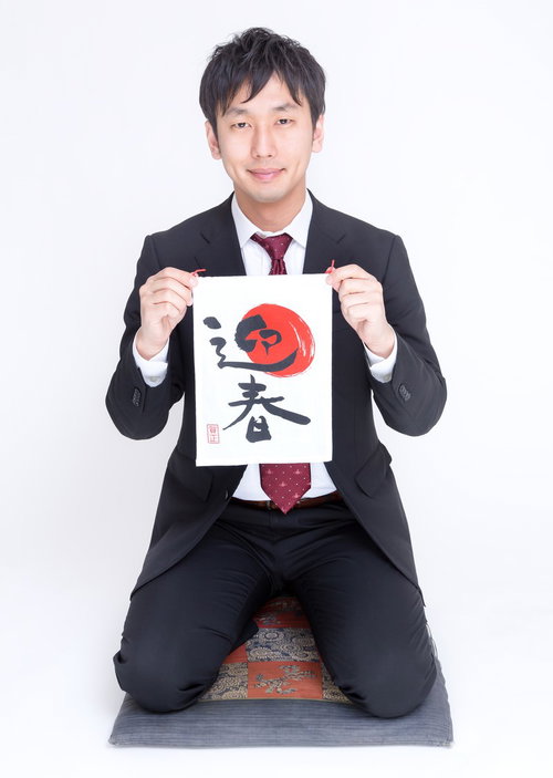 正座して「迎春」の書を掲げるスーツのビジネスマン