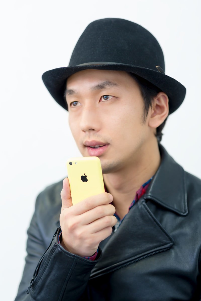 スマホを口元に近づけて演説する帽子の男性［モデル：大川竜弥］