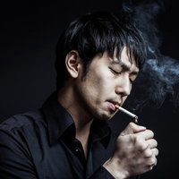 指先でタバコに火をつける男性の喫煙シーンの写真
