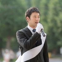 マイクを持って屋外でスピーチする政治家の写真