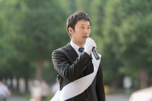 マイクを持って屋外でスピーチする政治家