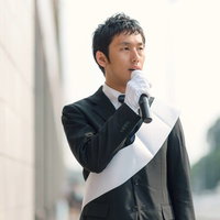 白い紙とマイクで街頭演説する立候補者の写真