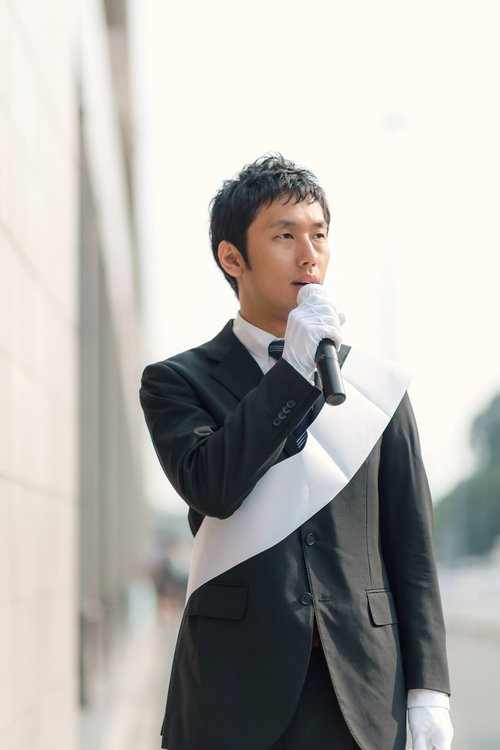 白い紙とマイクで街頭演説する立候補者