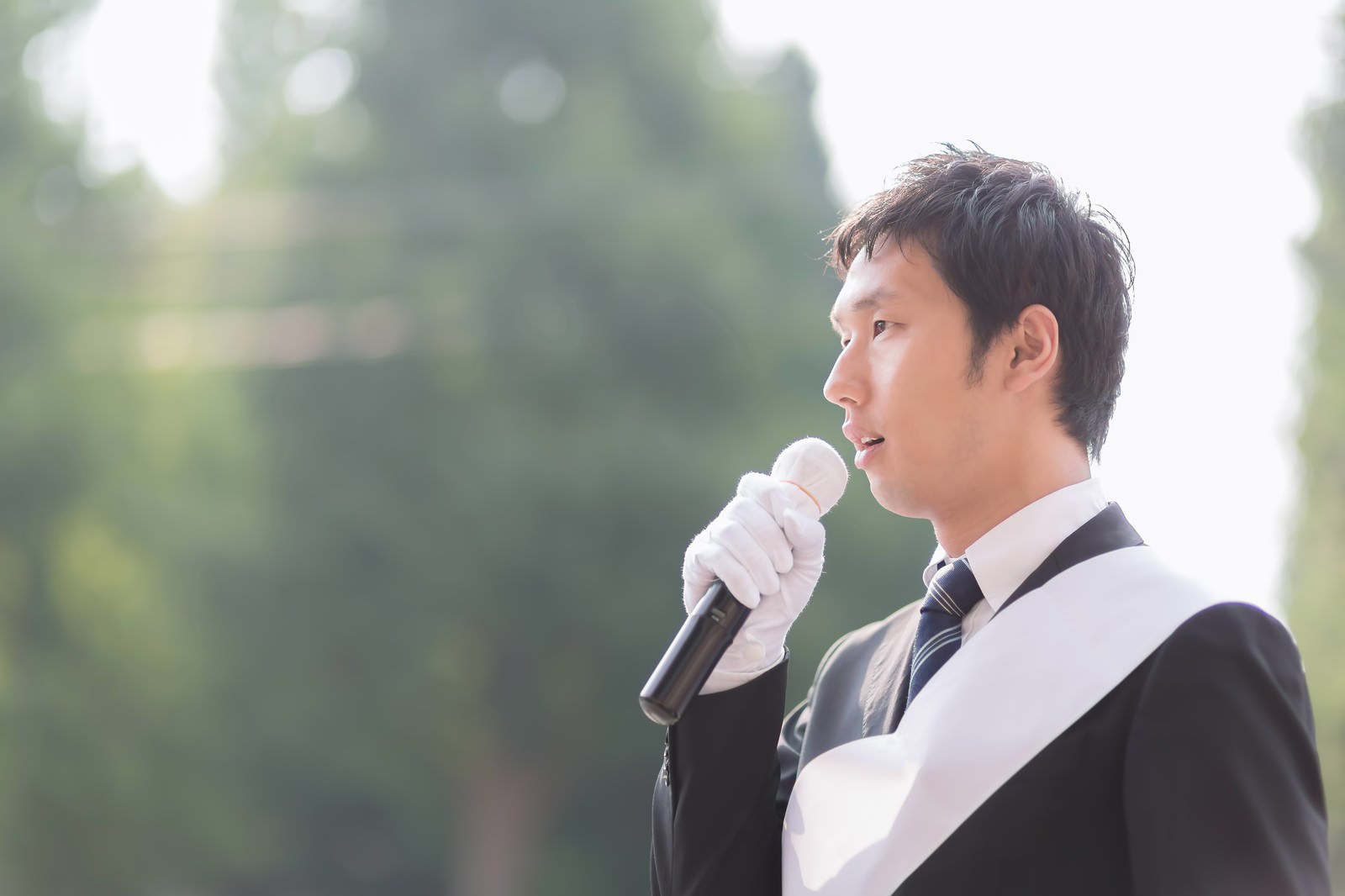 マイクを持って街頭演説する白い手袋の立候補者［モデル：大川竜弥］