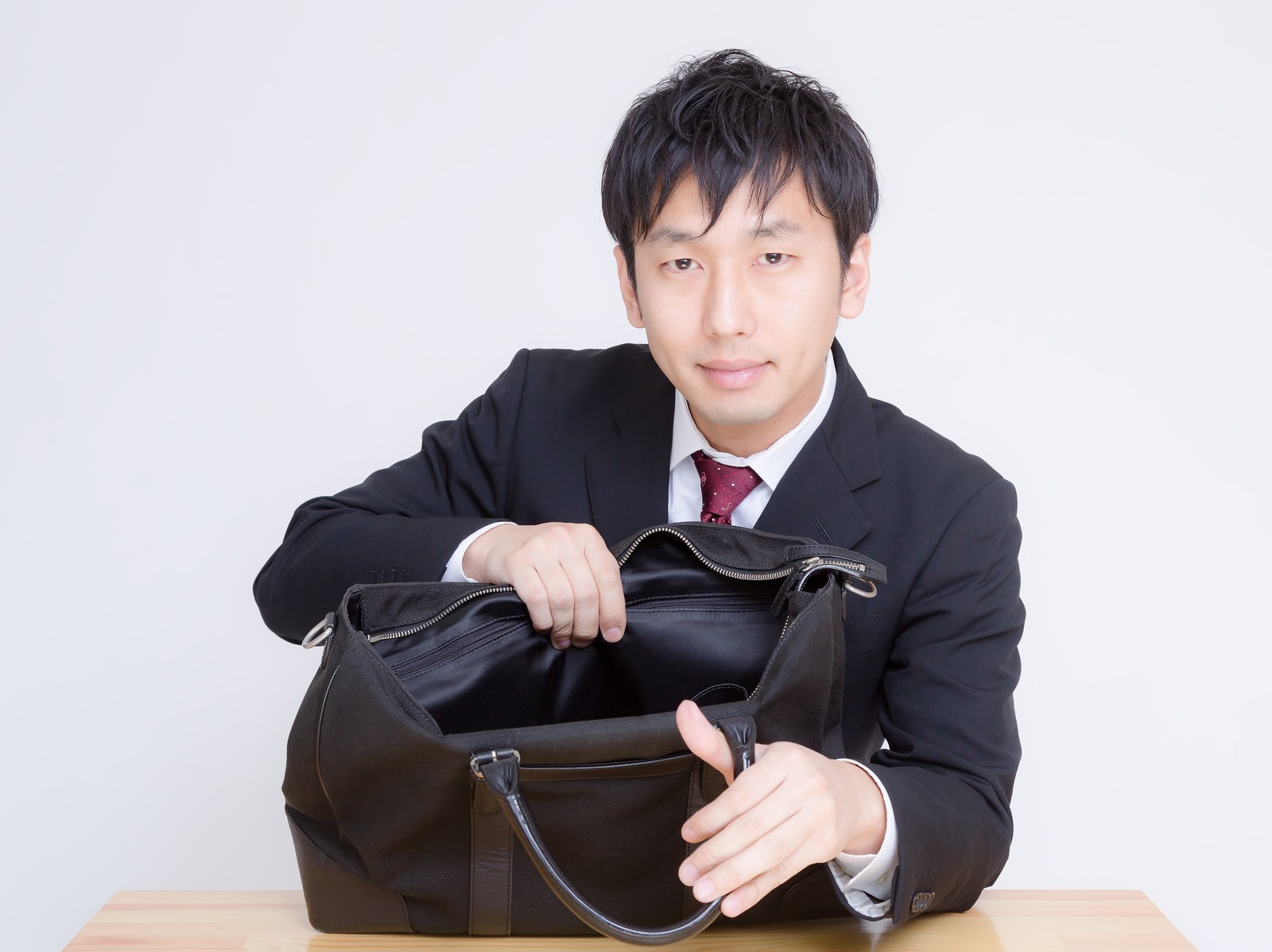 かばんを開けてカメラを見るスーツの男性［モデル：大川竜弥］