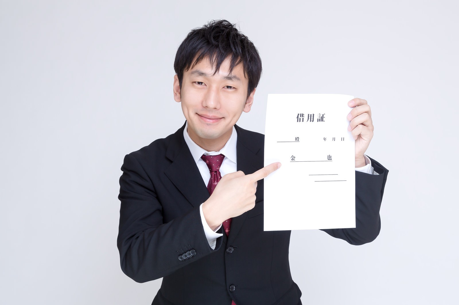 黒いスーツ姿の男性が白い借用証を掲げながら右手で指す［モデル：大川竜弥］
