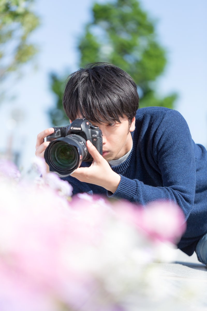 屋外で花を撮影する男性カメラマン［モデル：大川竜弥］