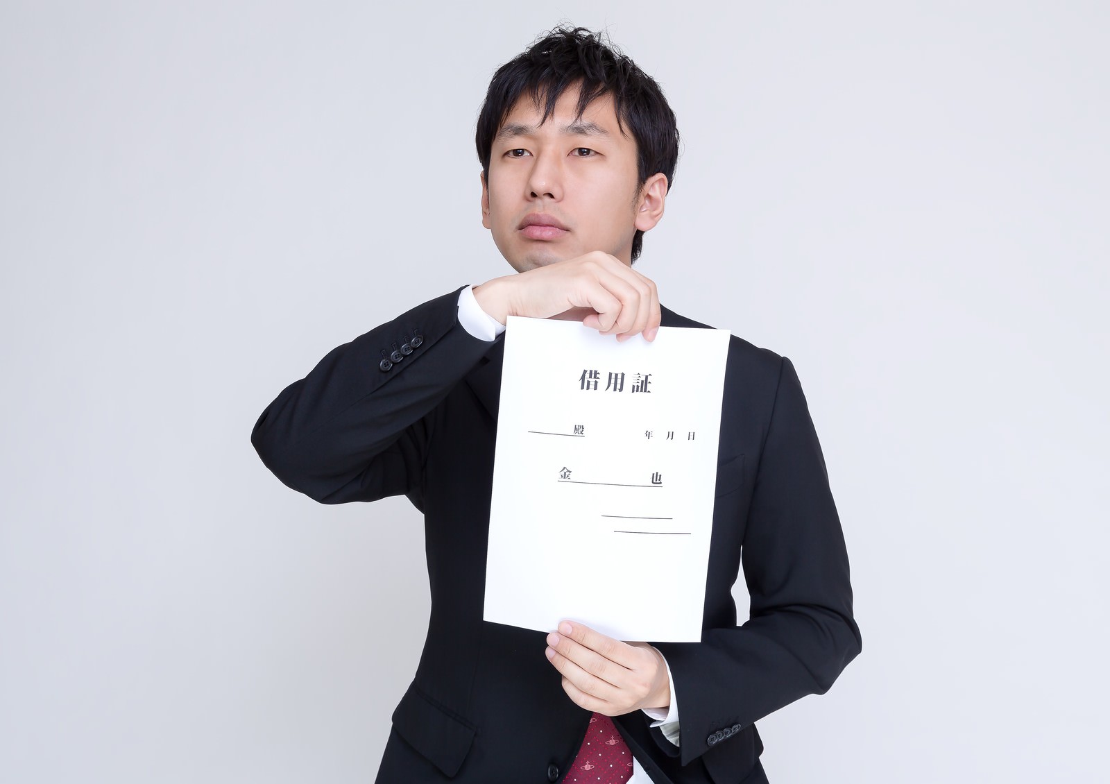 黒いスーツを着た男性が借用証を掲げて説明している写真［モデル：大川竜弥］