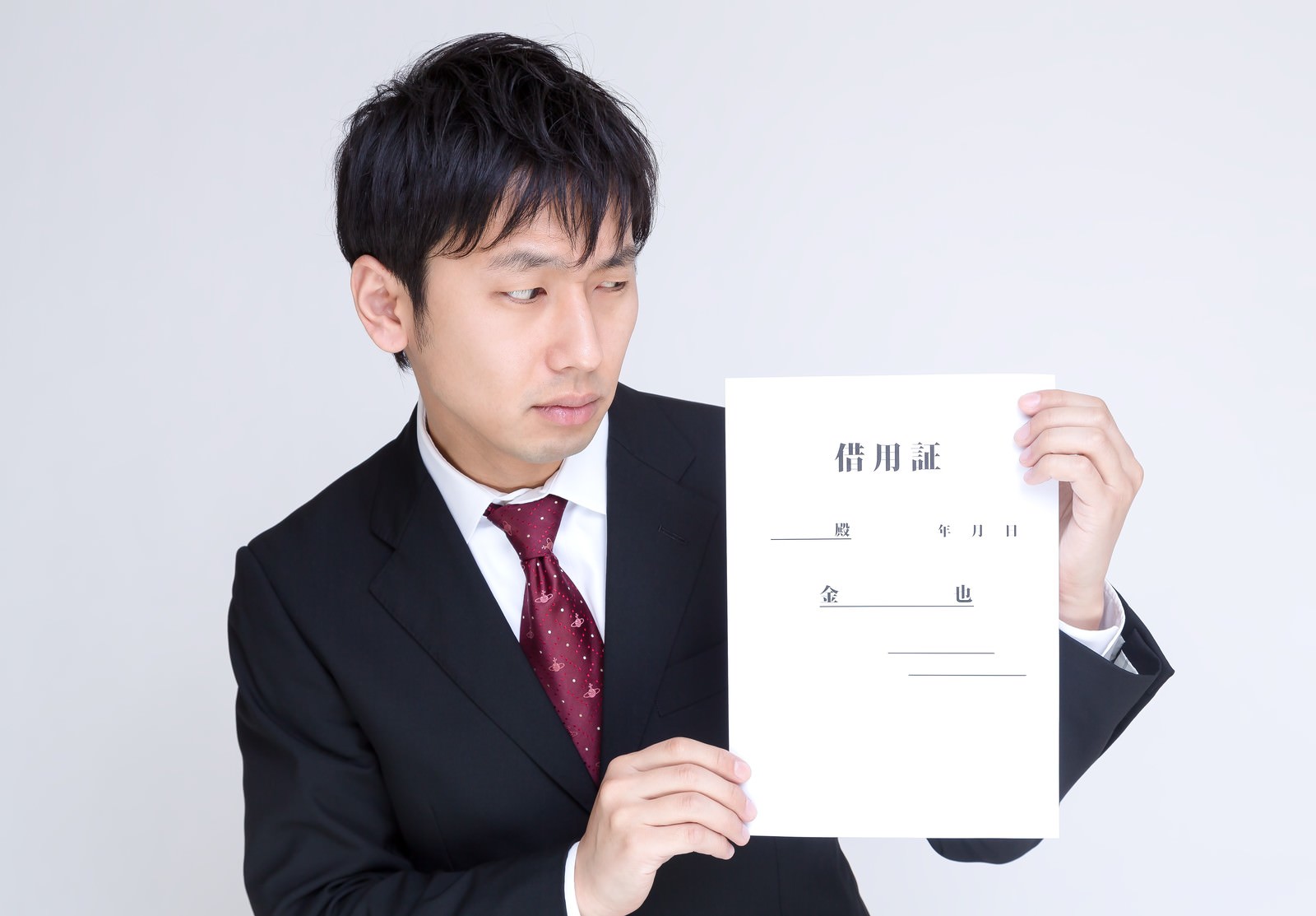 借用証を見つめ怪訝な表情を浮かべるスーツ姿の男性［モデル：大川竜弥］