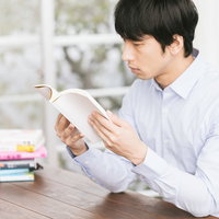 積ん読を処理する男性が机で手に取った本を読むの写真