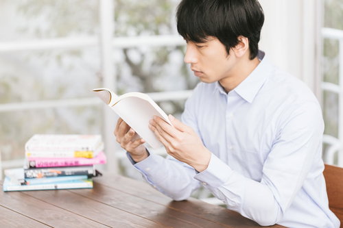 積ん読を処理する男性が机で手に取った本を読む