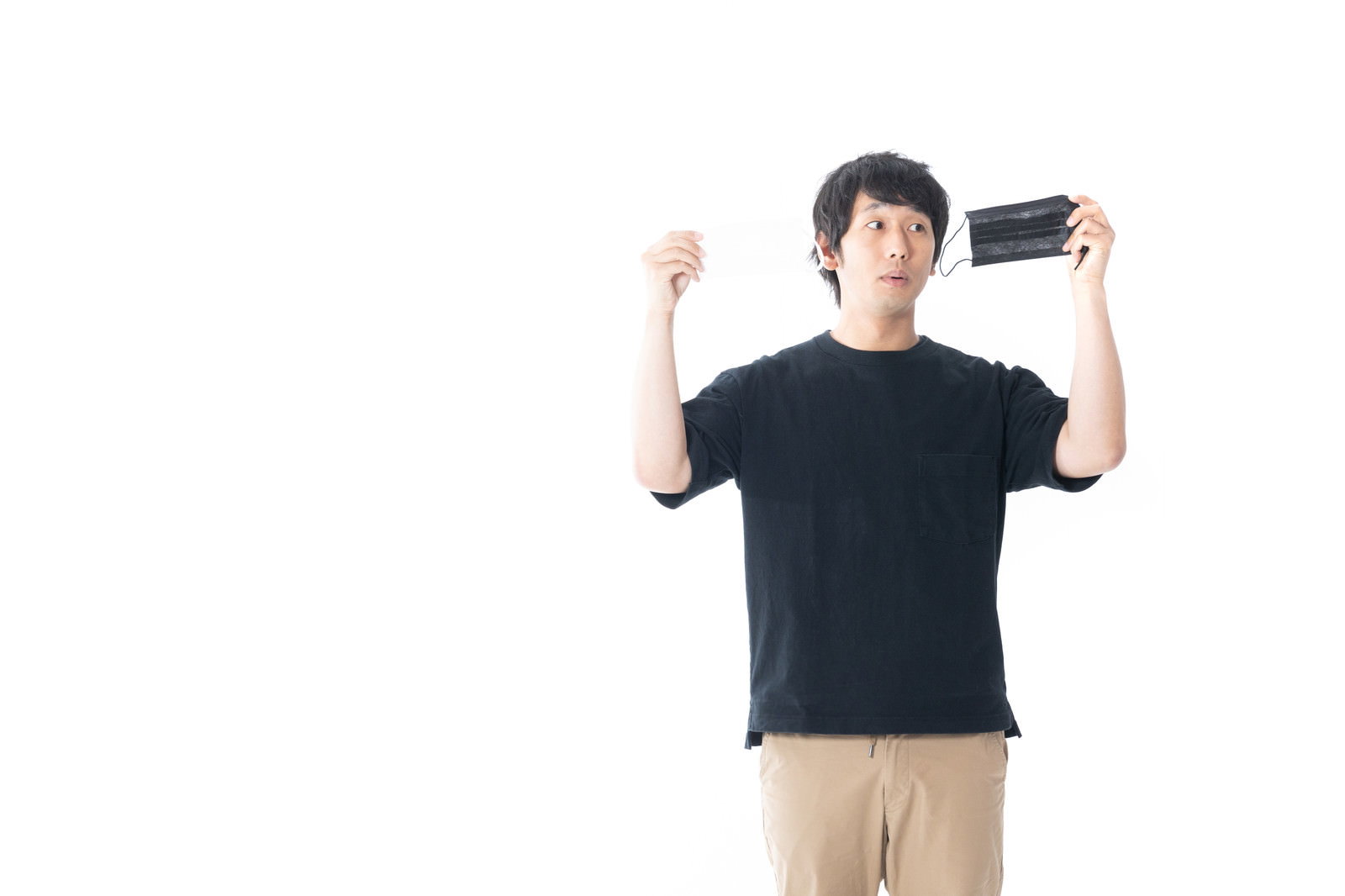 白い背景の前で黒いマスクを手に持つ黒Tシャツ姿の男性［モデル：大川竜弥］