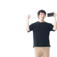 黒マスクを手に取る黒いTシャツの男性の写真