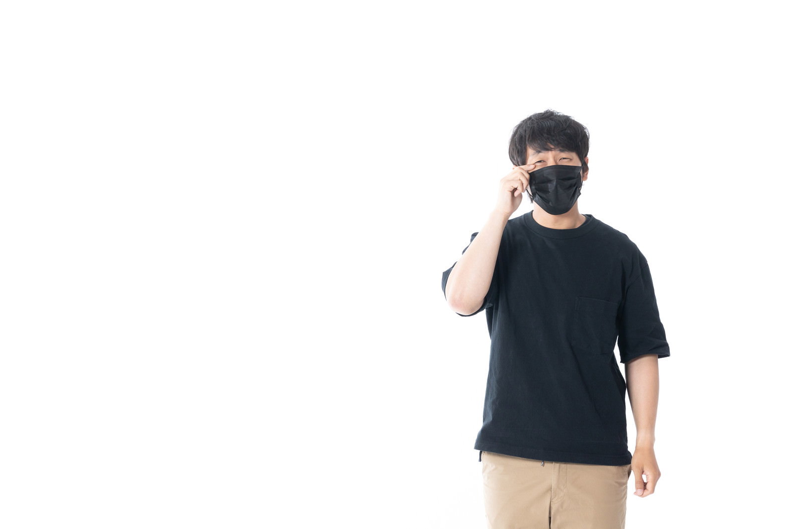 黒いマスクを着用し目元に手を当てて痒みを感じている男性［モデル：大川竜弥］