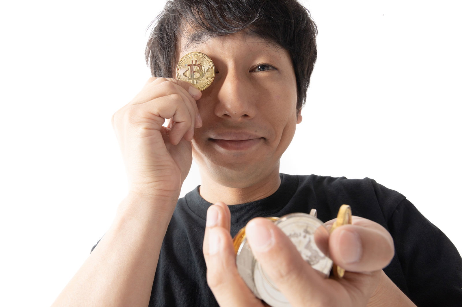 ビットコインのコインを手に持ち、片手で目元に当てる男性［モデル：大川竜弥］