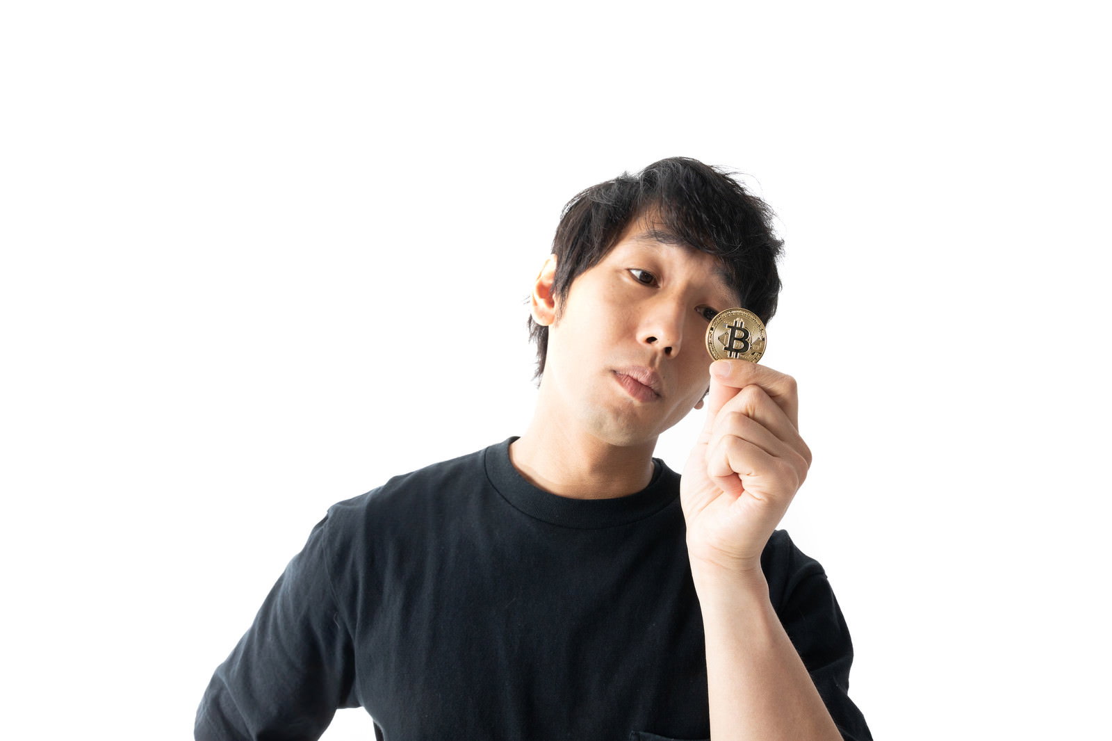 ビットコインのシンボルを手に持ち見つめる黒いTシャツの男性［モデル：大川竜弥］