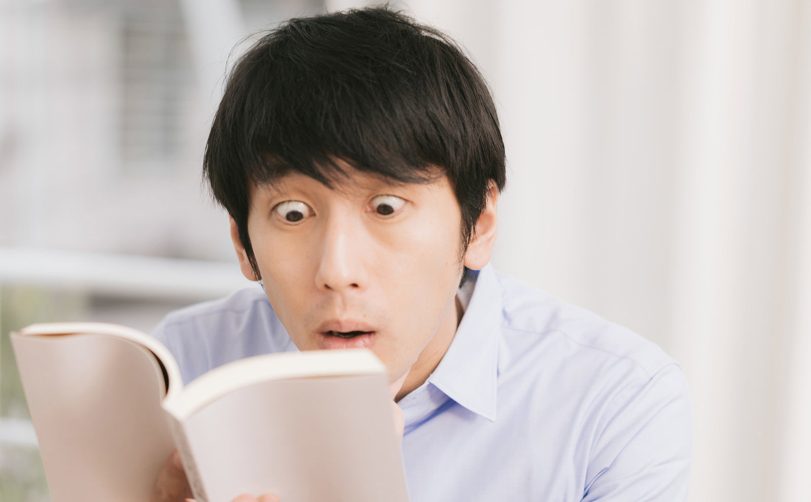 本の誤植を見つけて目を見開く男性［モデル：大川竜弥］