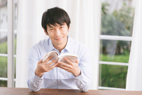 書評記事を執筆するプロブロガー男性が本を手に笑顔