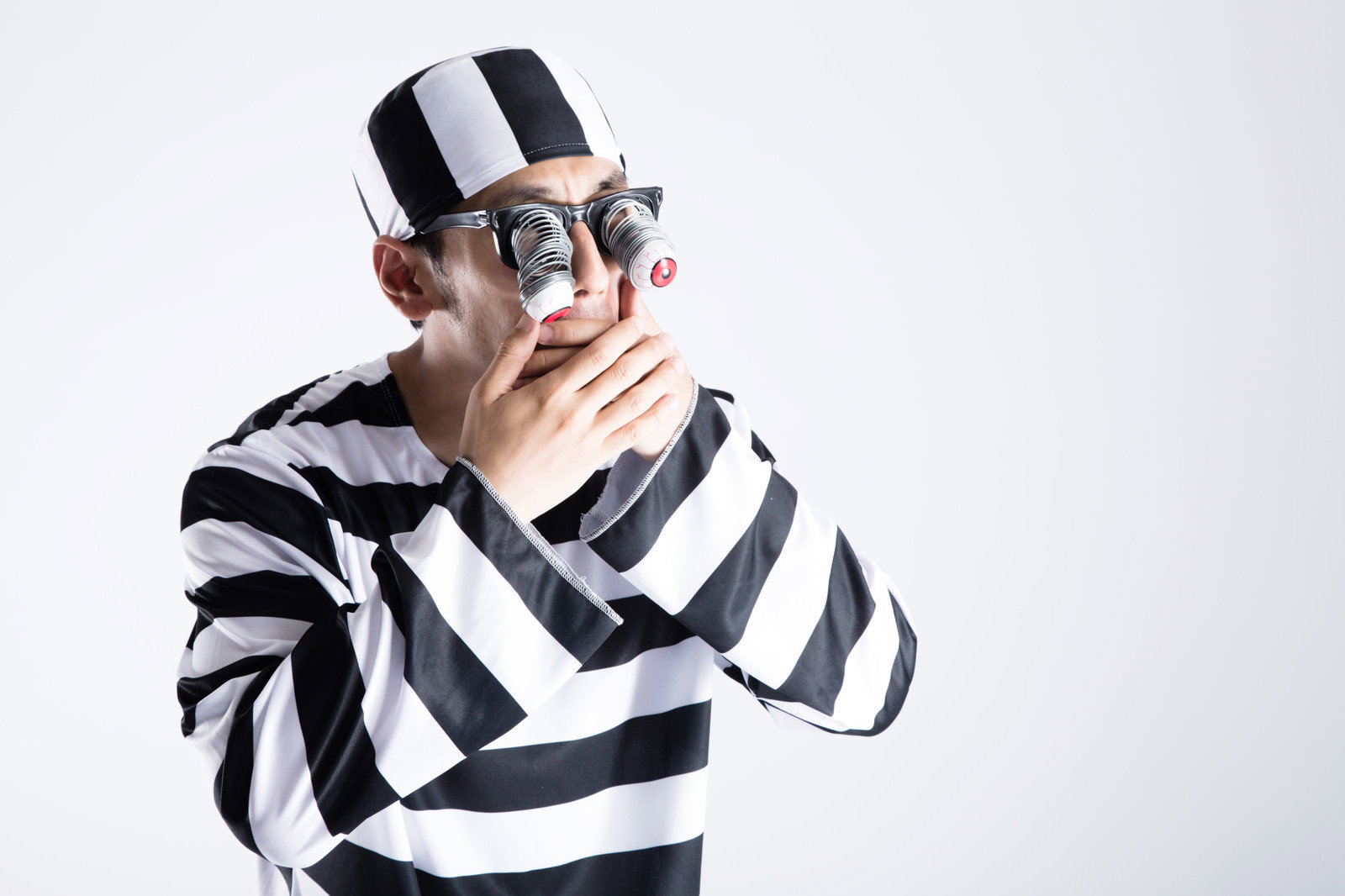 黒白ボーダー囚人衣装を着た男性が目玉飛び出し双眼鏡を持ち、驚いた顔で横を向いている［モデル：大川竜弥］