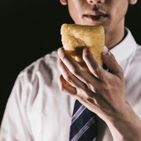 6インチサイズのあぶらあげをほおばるサラリーマンの写真
