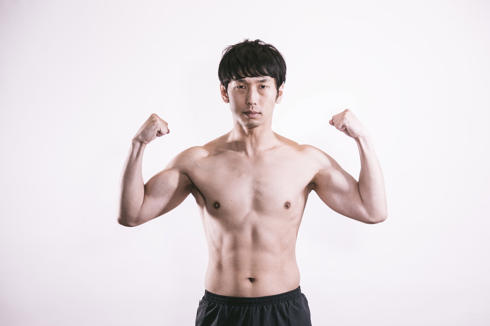 力こぶを作って筋肉をアピールする上半身裸の男性［モデル：大川竜弥］