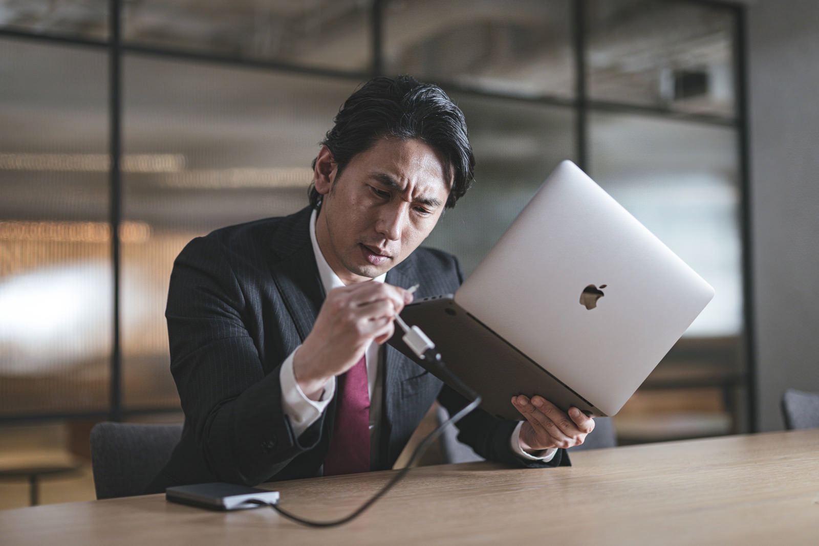 ノートパソコンを前にしてUSBケーブルの接続に困っている会社員の男性［モデル：大川竜弥］