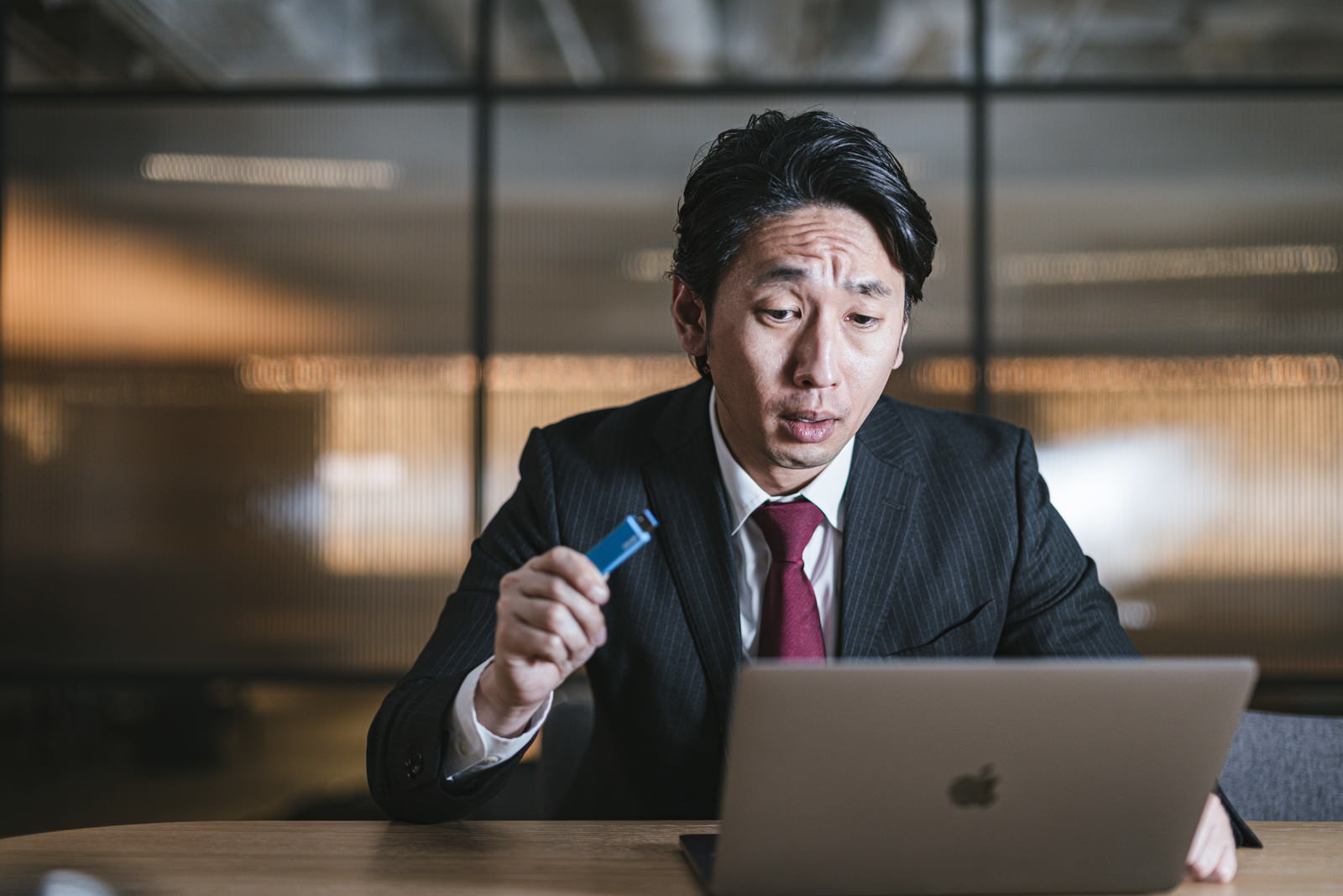 USBメモリを握りしめて脅迫的な表情を見せる会社員男性［モデル：大川竜弥］