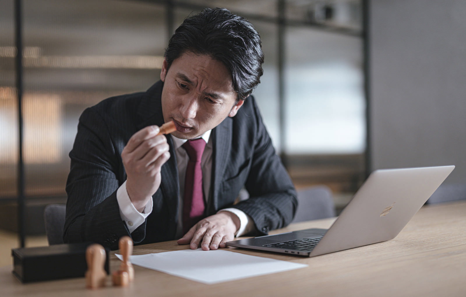 契約書の前で困った表情を見せるスーツ姿の男性役員［モデル：大川竜弥］
