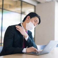 肩こりの原因、それは幽霊のしわざです〜会議中にマスク姿の男性が肩を押さえるの写真